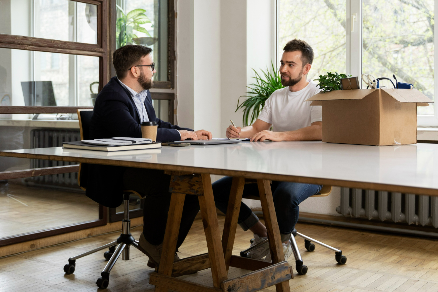 Two men discussing property sharing agreements in a modern office setting, with documents and a cardboard box on the table, emphasizing legal consultation and collaboration.