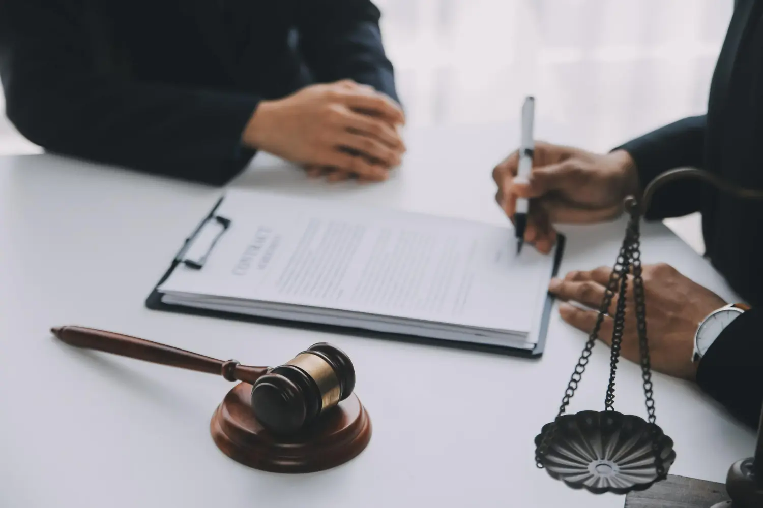 Lawyer signing contract on table with gavel and legal scale, representing business litigation and legal services.