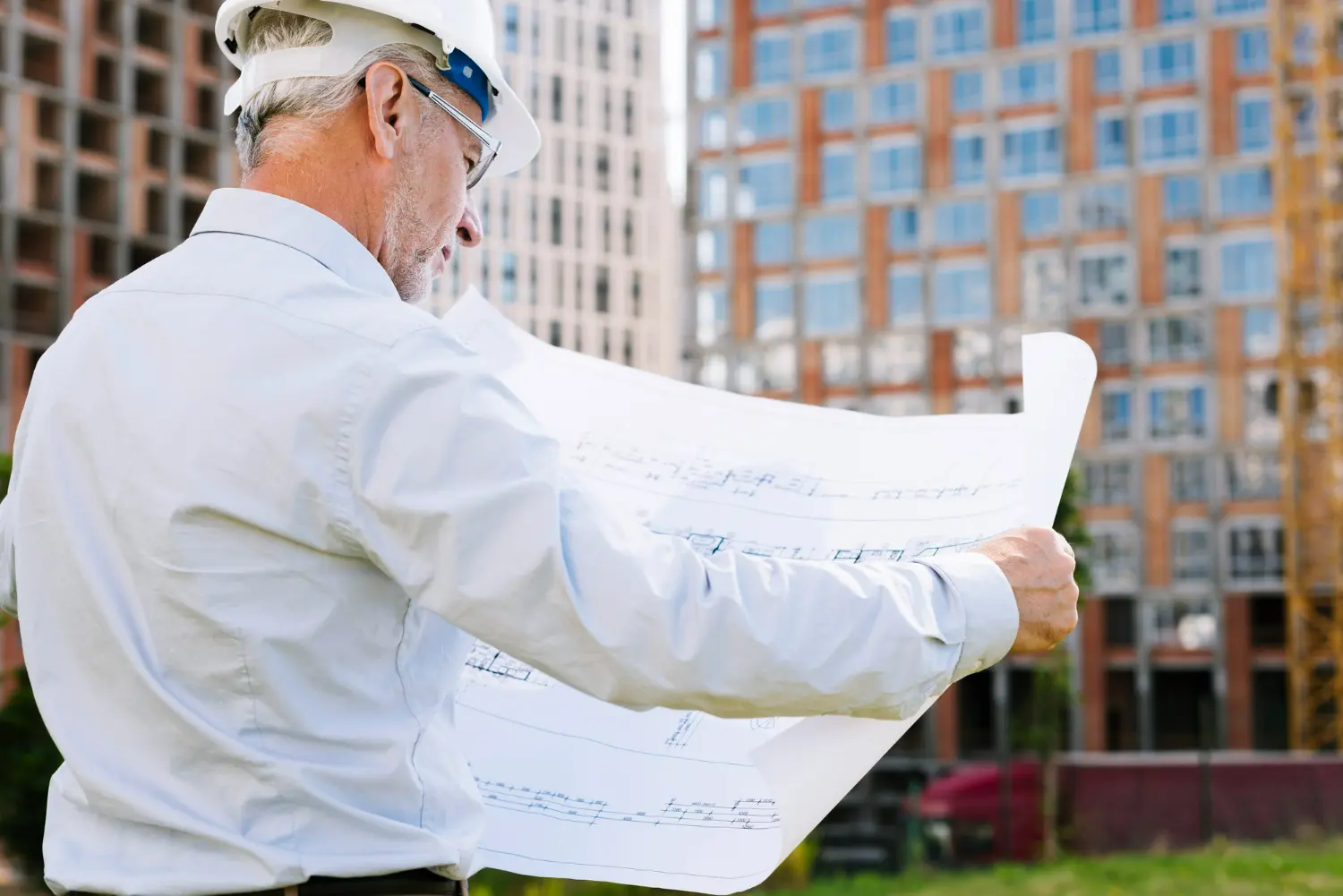 Construction professional examining building plans outdoors, with urban development in the background, relevant to zoning laws and real estate regulations.