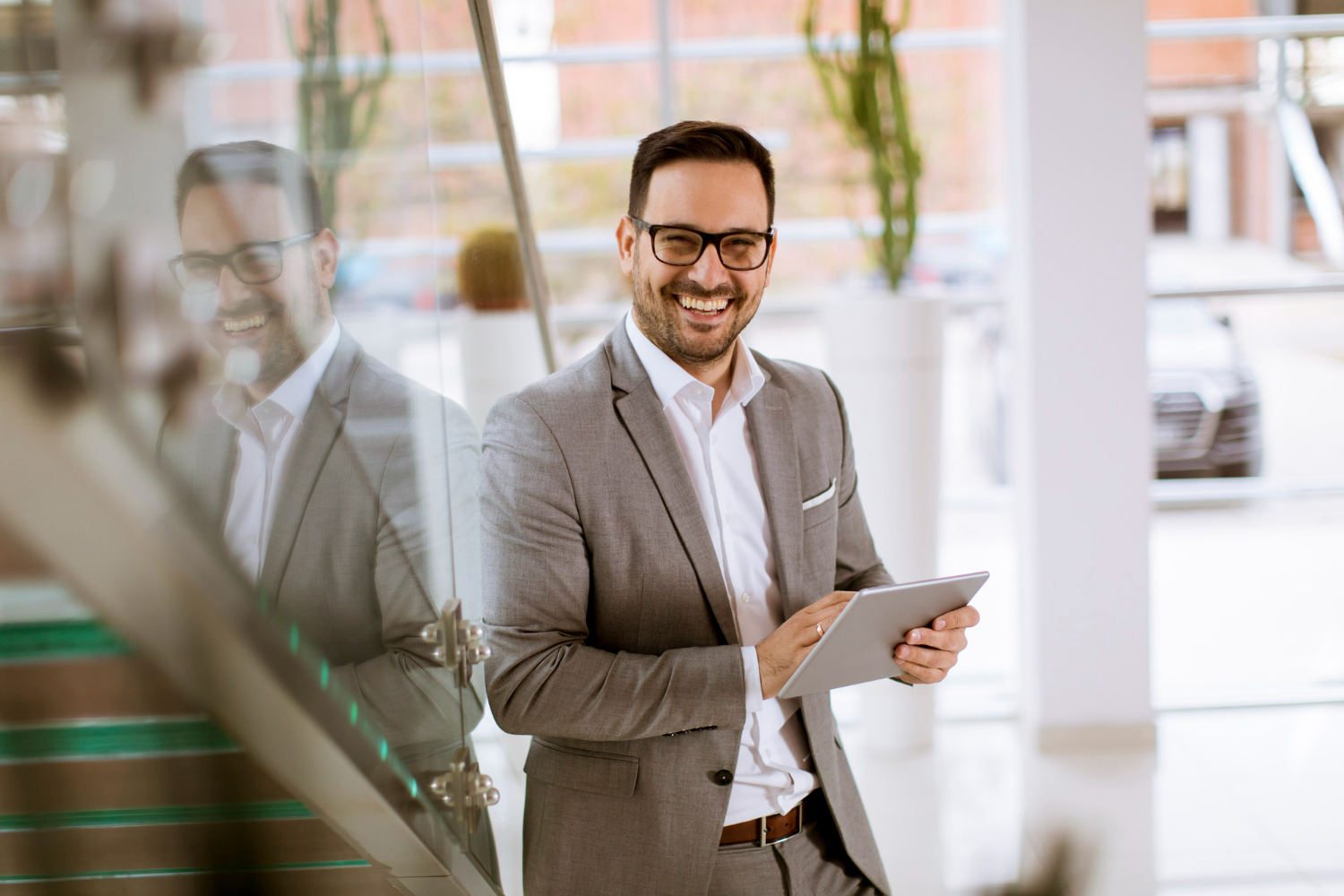 Smiling professional in a gray suit holding a tablet, standing in a modern office environment, reflecting the legal expertise of Dillon, Miller, Ahuja & Boss LLP in real estate transactions.