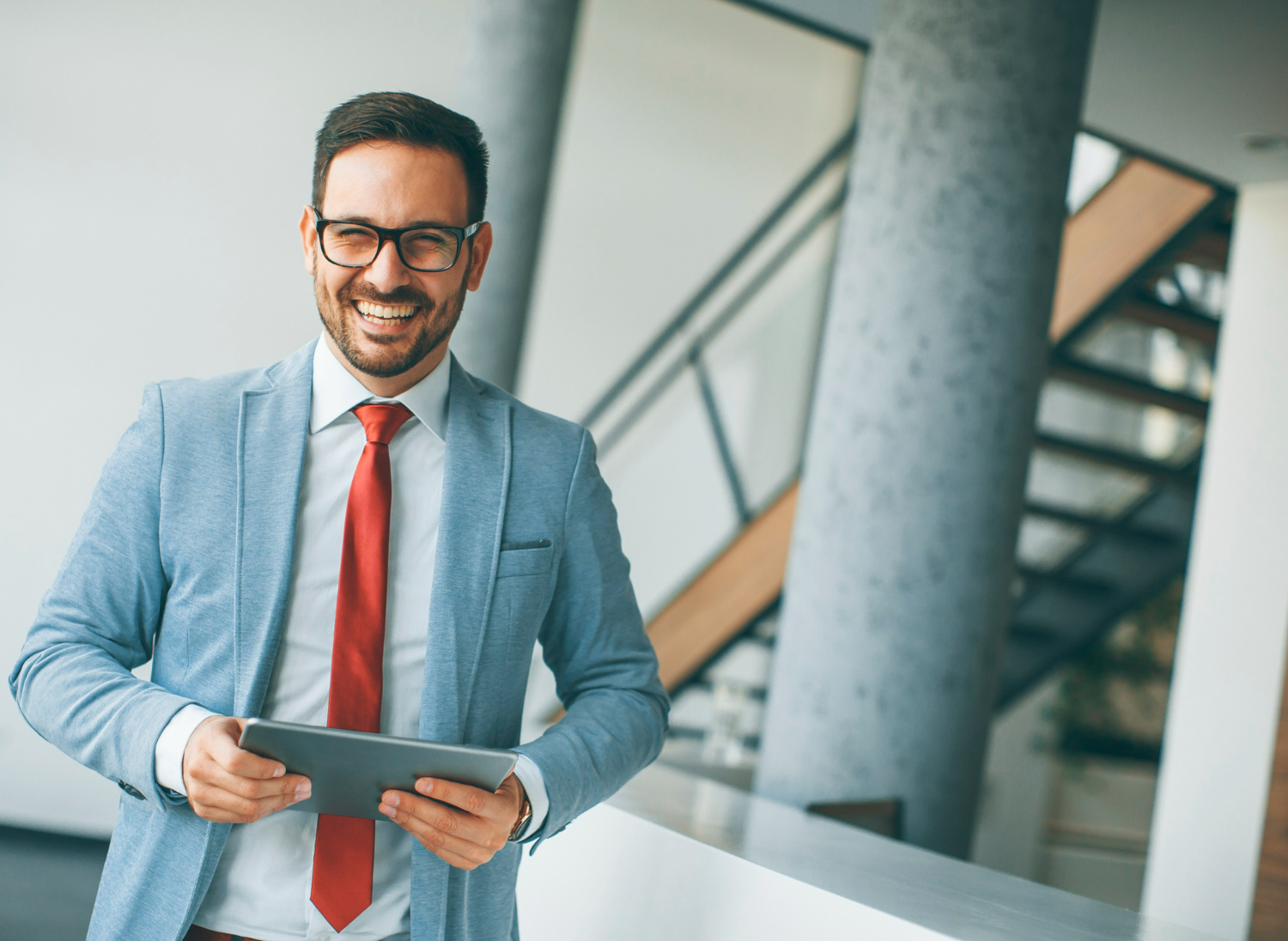 Smiling businessman in a light blue suit and red tie holding a tablet, representing legal support for LLC formation in California.