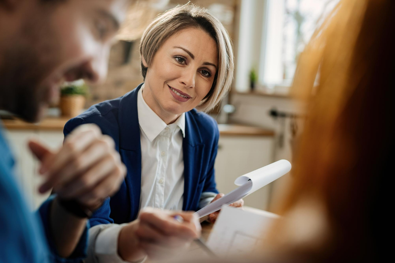 Professional woman in a blue blazer discussing real estate documents with clients, emphasizing legal guidance in transactions and negotiations.