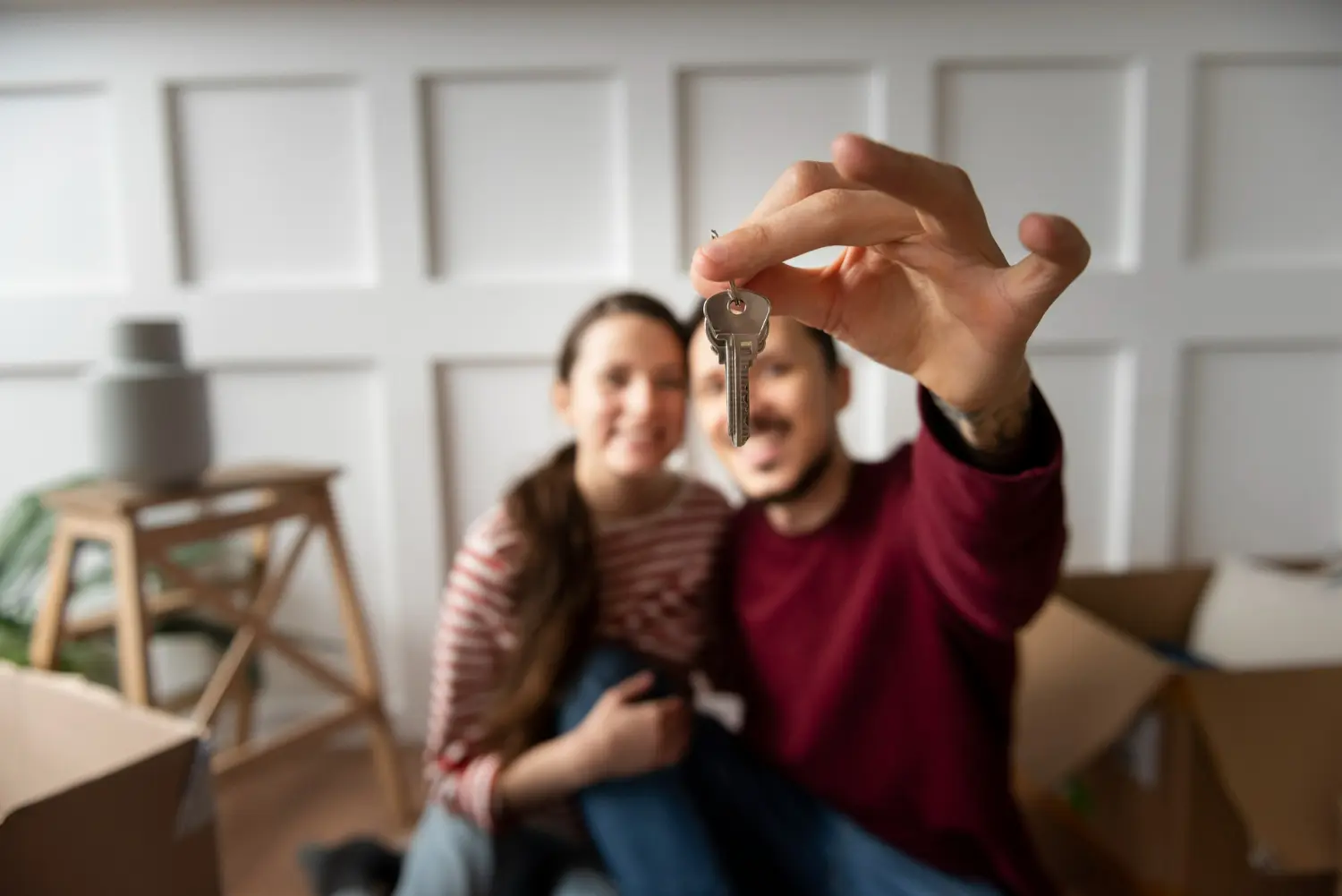 Couple celebrating homeownership, holding keys in front of moving boxes, symbolizing property purchase and legal ownership.