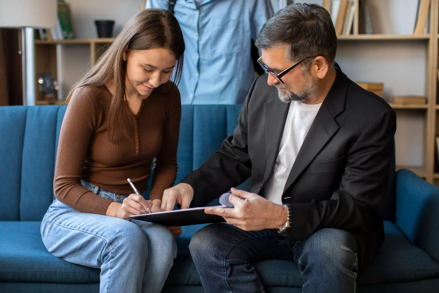 Man and woman discussing and signing lease agreement on a couch, emphasizing negotiation and documentation in lease conflict resolution.