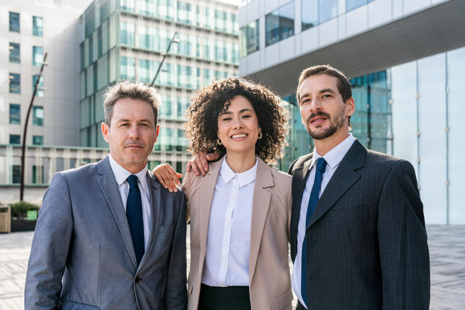 Professional team of three lawyers in business attire, smiling confidently outdoors in front of a modern building, representing DMAB law firm in Carlsbad.