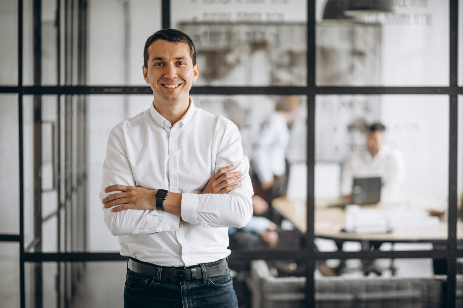 Smiling professional man in a white shirt with arms crossed, standing in a modern office setting, emphasizing proactive legal planning and business strategy.