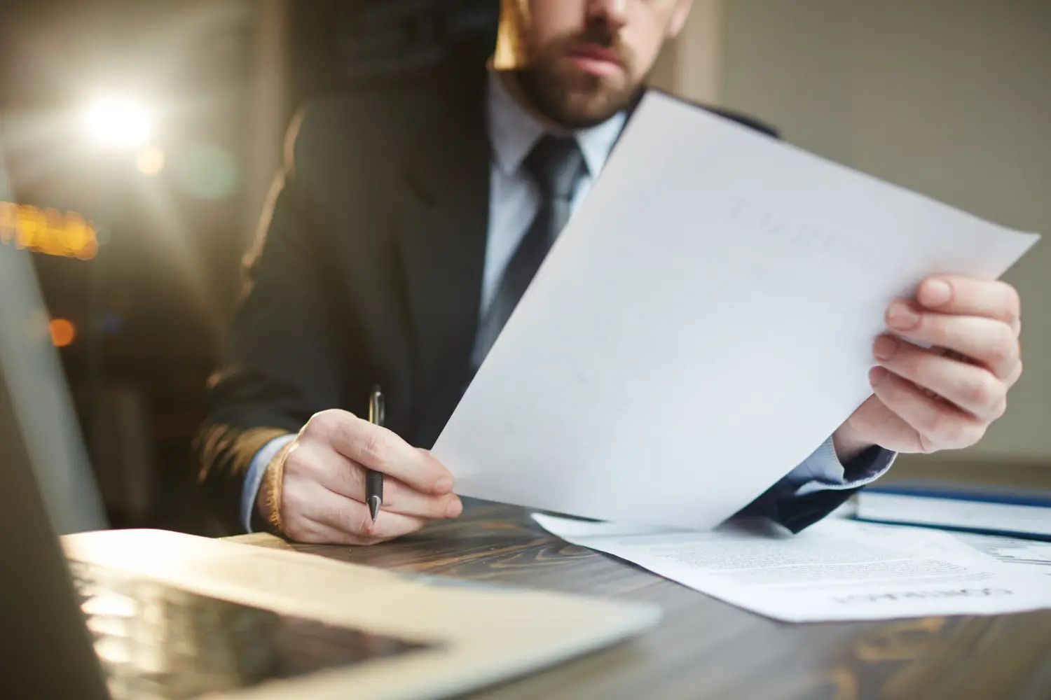 Business professional reviewing documents with a pen, laptop, and additional paperwork on a wooden table, illustrating the process of managing escrow and closing in California commercial transactions.