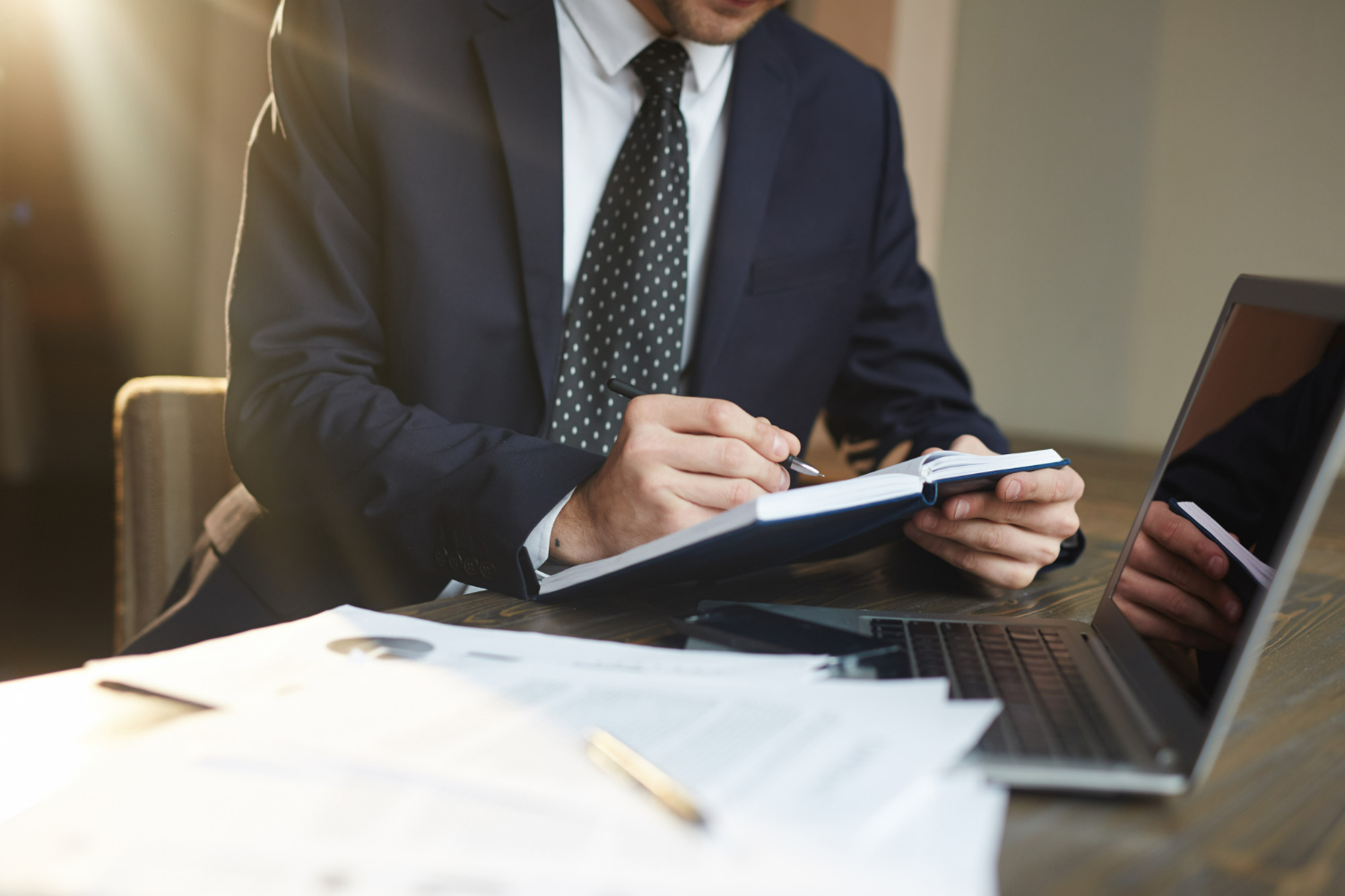 Businessman in a suit taking notes beside a laptop, illustrating careful legal planning for commercial property purchases in Carlsbad
