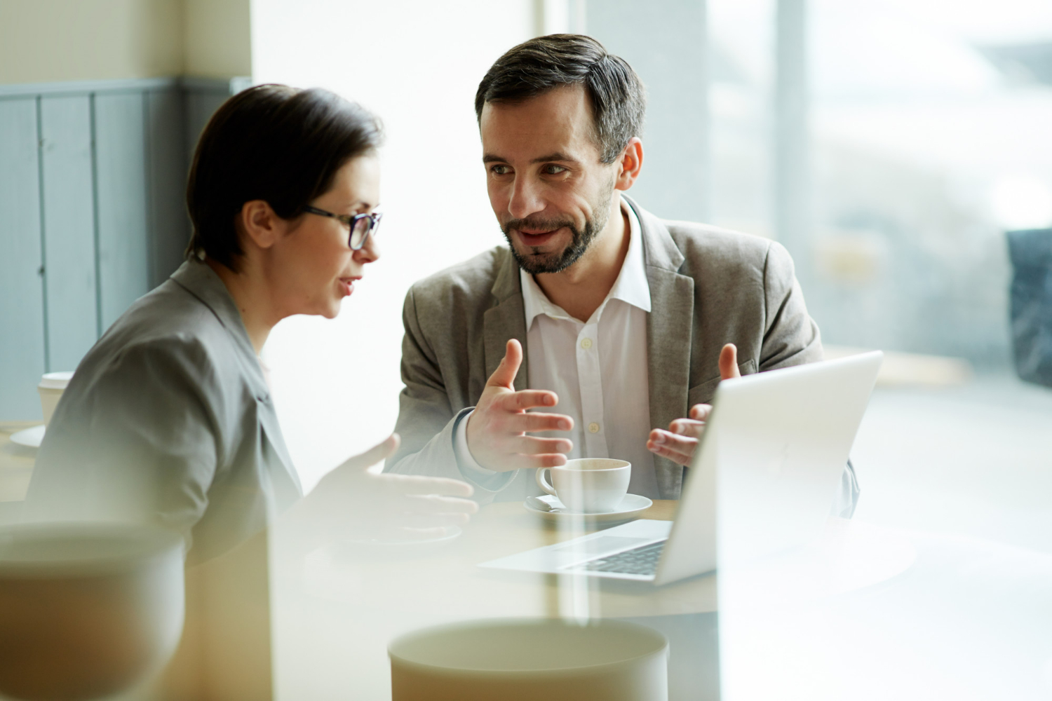 Business professionals discussing partnership dissolution and legal remedies over a laptop in a caf&eacute; setting.