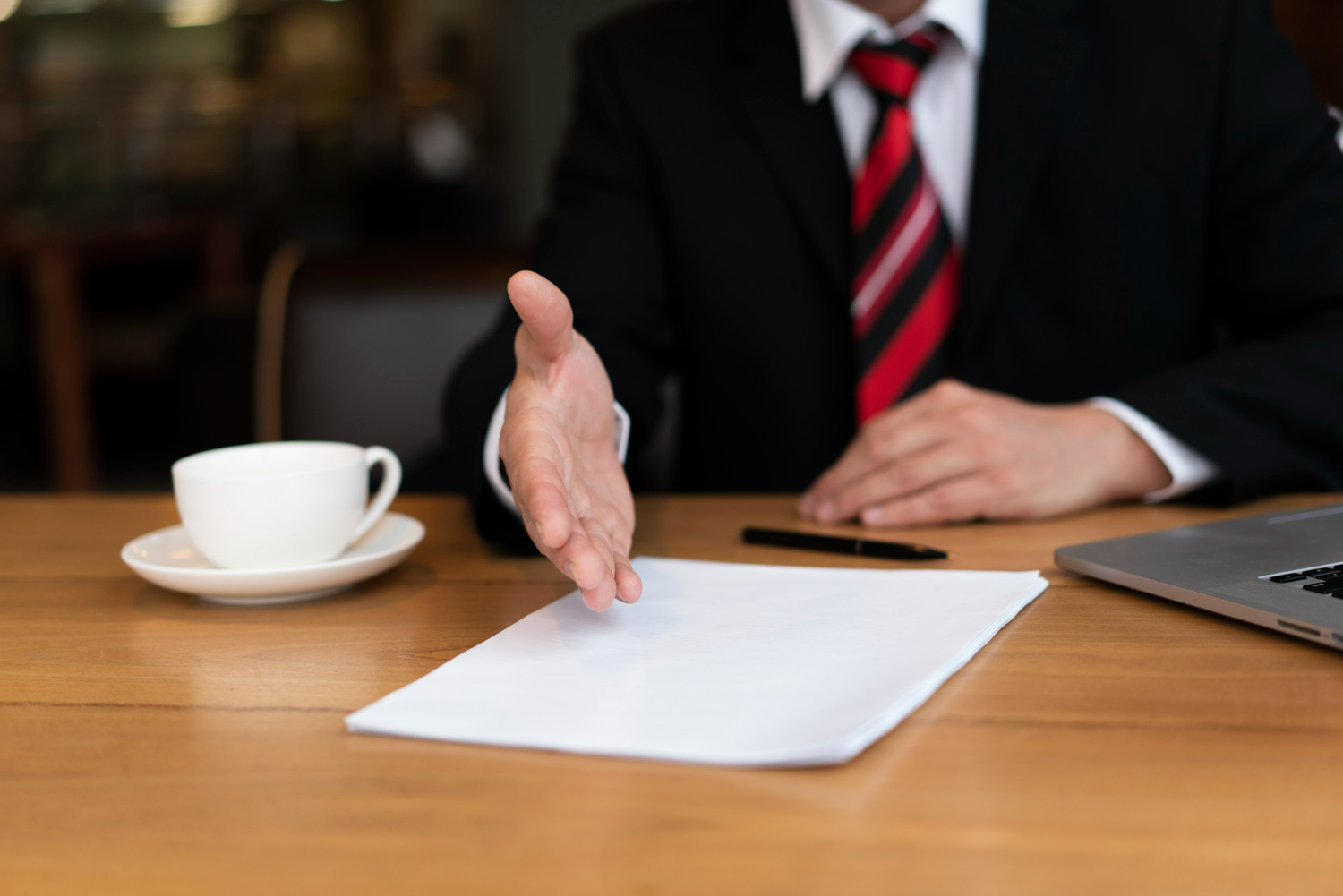 Business attorney gesturing towards a document on a table, with a cup and laptop nearby, illustrating discussions on Non-Disclosure Agreements (NDAs) and confidentiality.