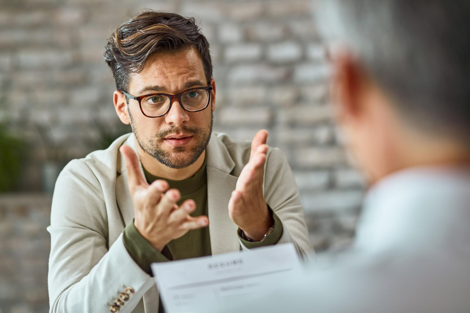 Man in a light blazer discussing business matters, emphasizing points with hand gestures, during a consultation about non-disclosure agreements (NDAs) in a professional setting.