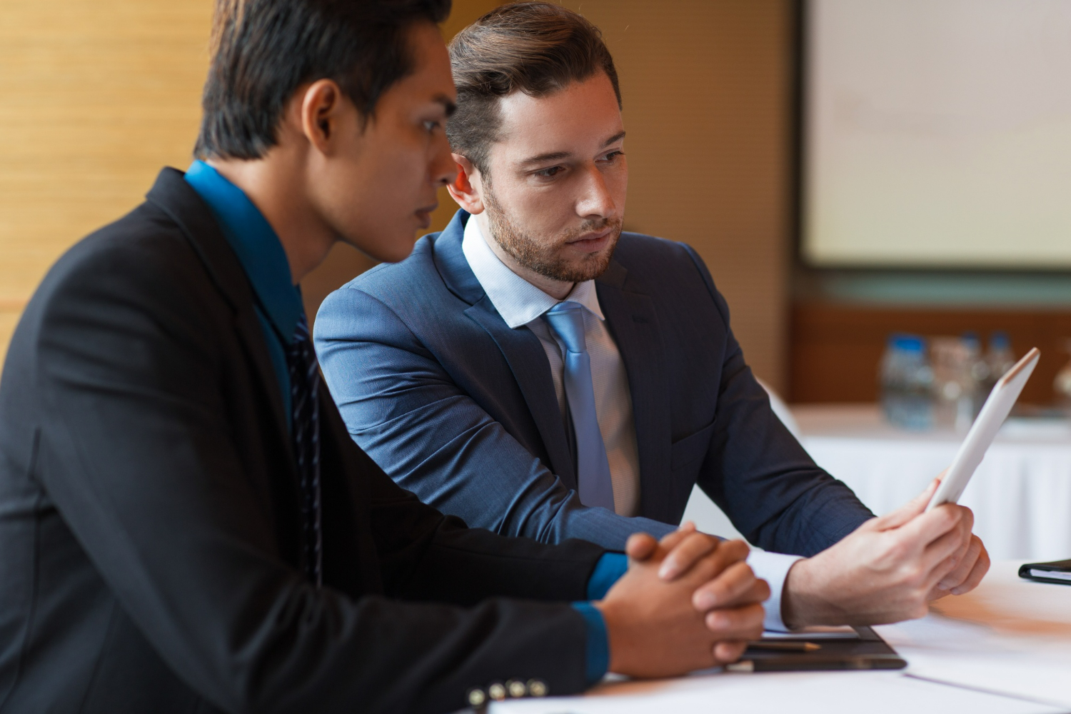Two business professionals in formal attire engaged in a serious discussion, one holding a document, emphasizing the importance of consulting a business attorney for partnership agreements and investment decisions.