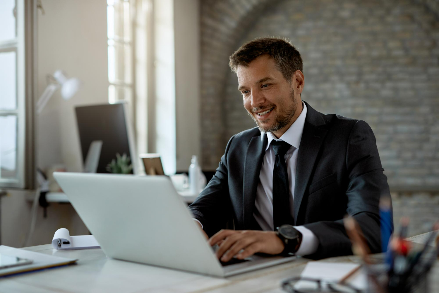 Business professional in a suit working on a laptop at a desk, illustrating legal and business services related to company secret protection.