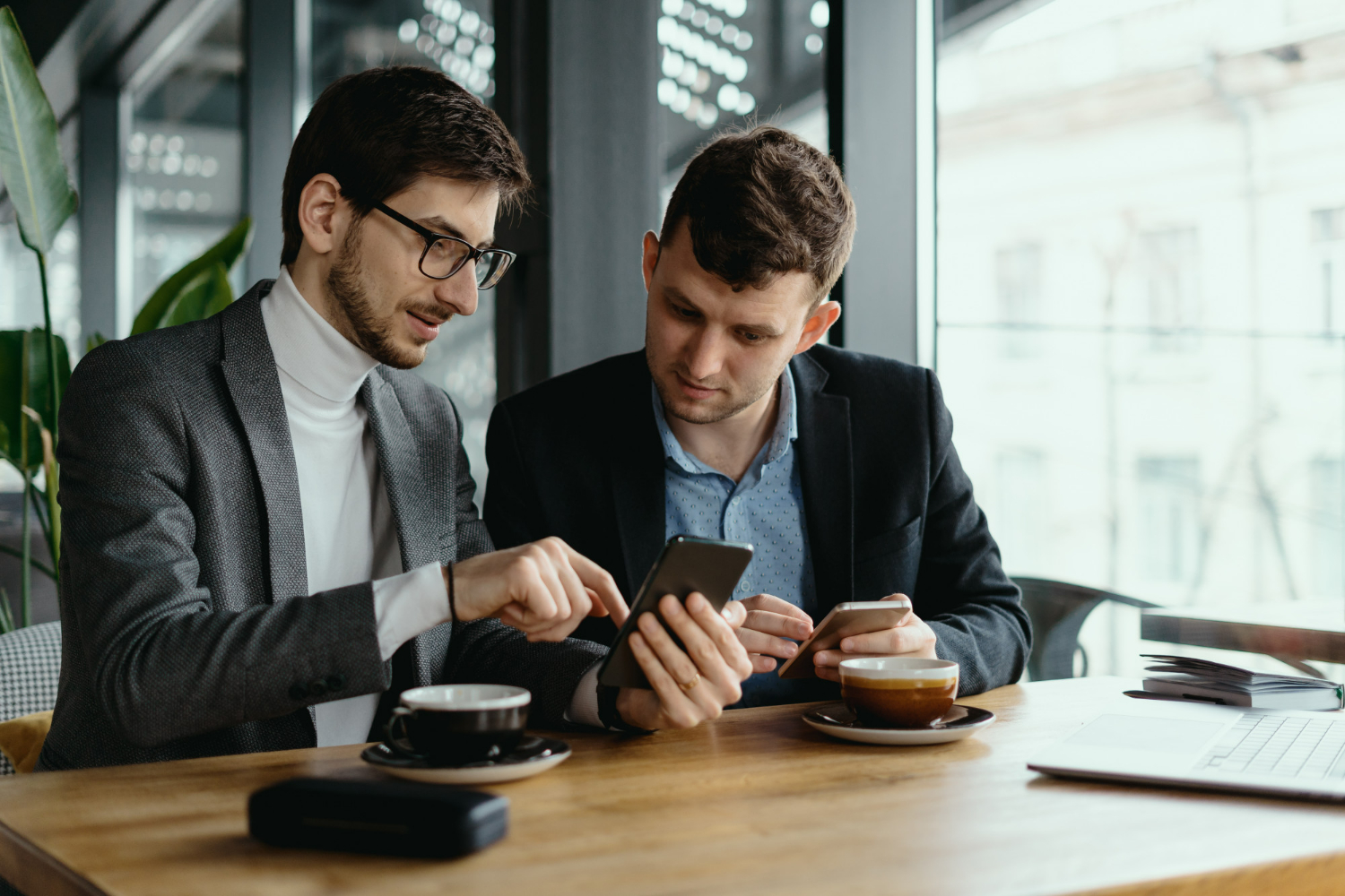 Two business professionals reviewing information on a smartphone while meeting at a table with coffee, representing early-stage transaction discussions with a business attorney.