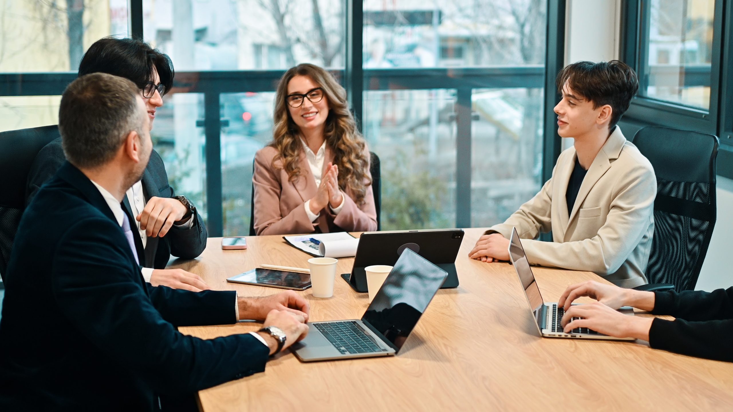 A diverse group of professionals in business attire collaborates around a conference table with laptops and documents while discussing options to change their business structure