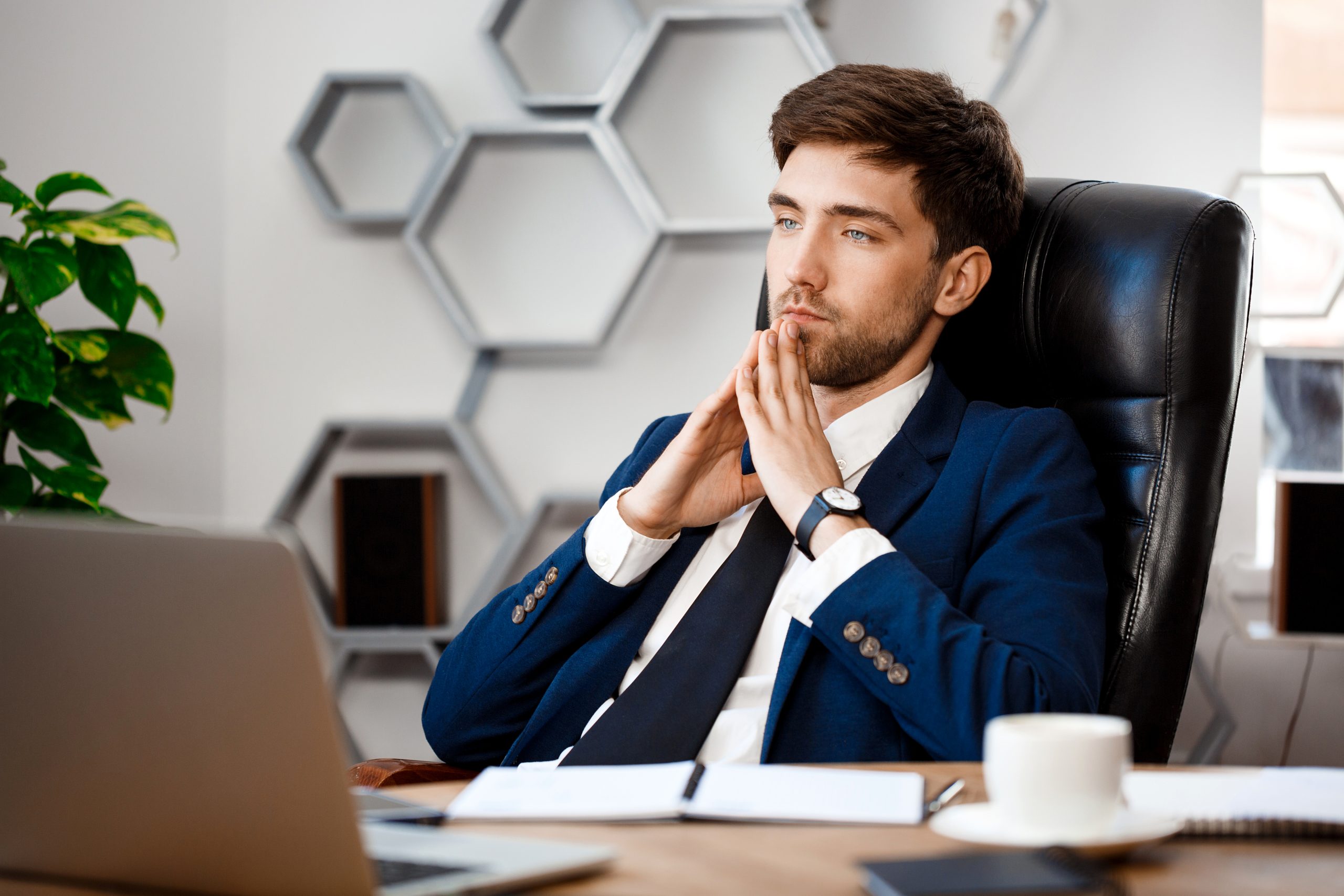 A thoughtful business owner in a suit sits at a desk with fingers interlocked, pondering whether to change their business structure