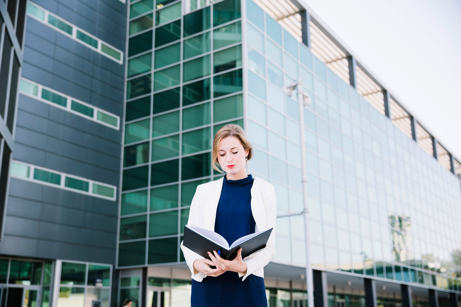 A business professional reviewing documents outside a modern office building, representing the legal evaluation process involved in choosing between purchasing or leasing commercial property