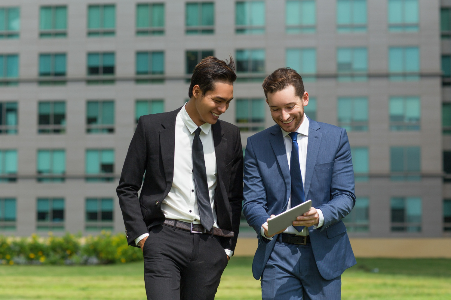 Two business partners walking outdoors while reviewing a tablet, symbolizing collaboration and the evolving nature of business relationships as companies grow