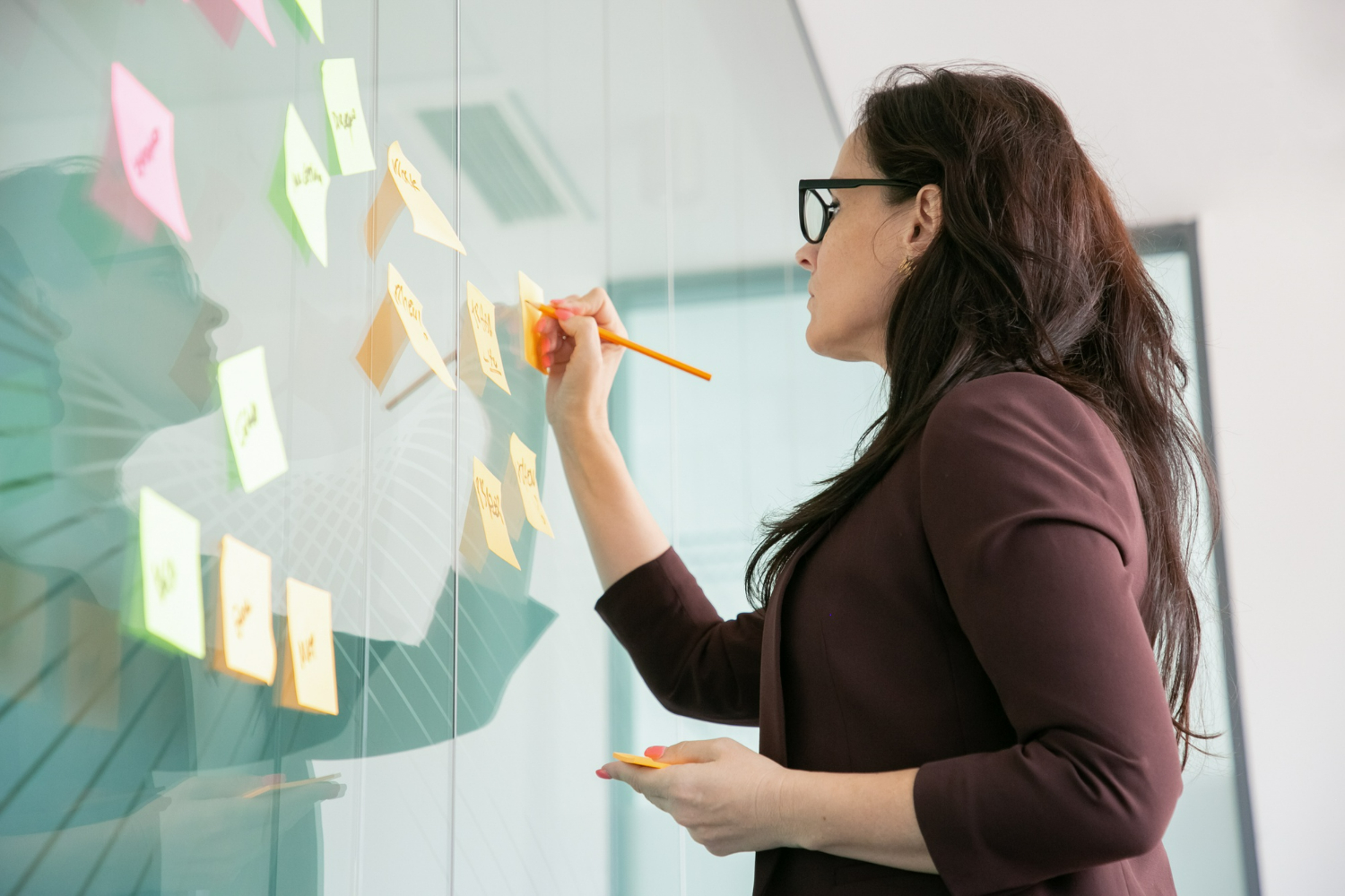 Businesswoman brainstorming and organizing ideas on a glass wall with sticky notes
