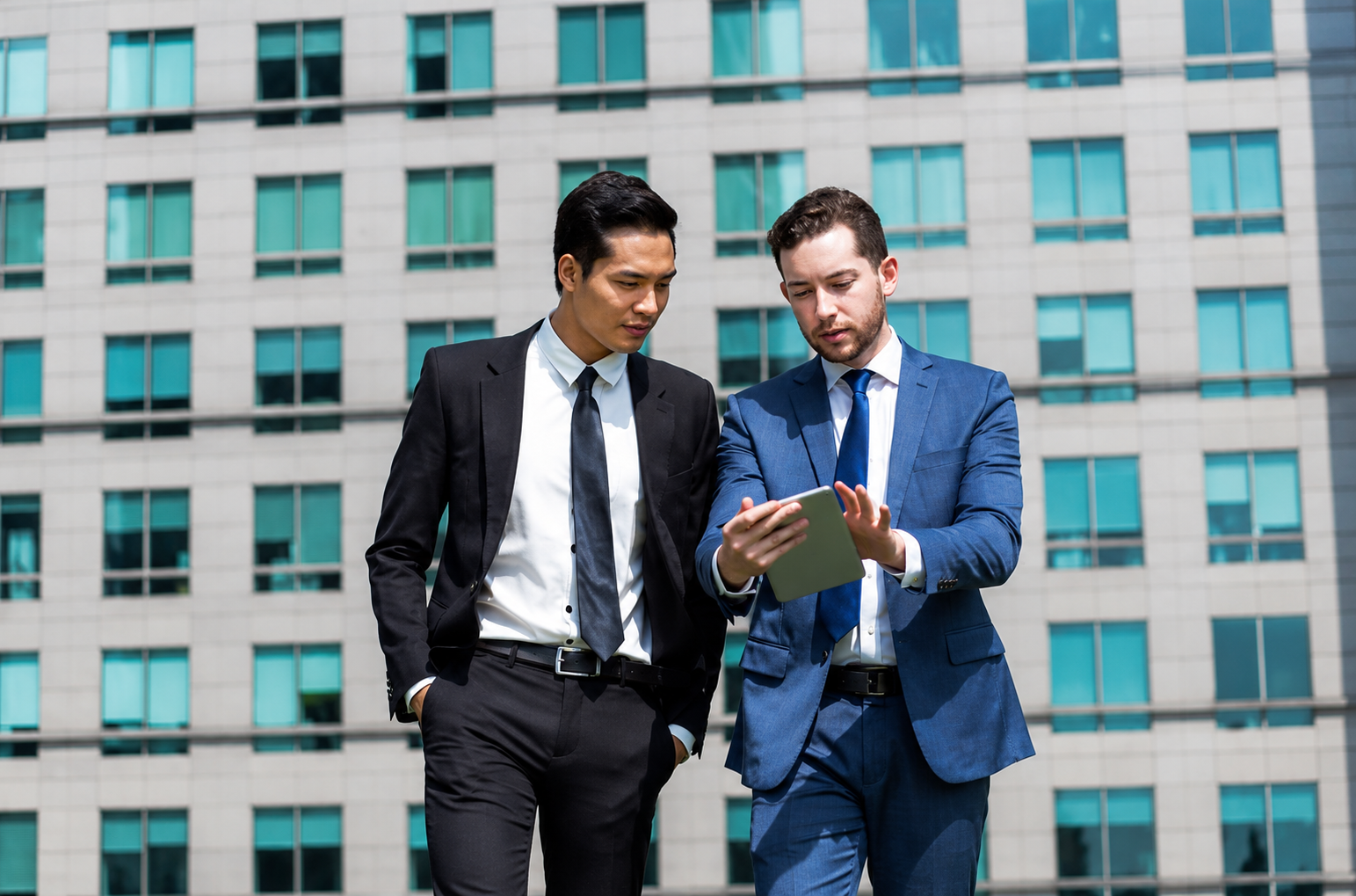 Two business partners in suits reviewing information on a tablet outside a commercial building, representing a California business partnership discussion